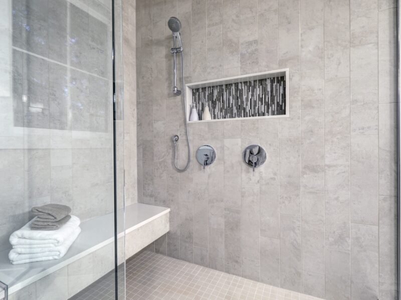 Shower Remodel Matthews, NC: Glass walk-in shower featuring gray subway tile surround and a decorative mosaic tile stripe in the wall niche.